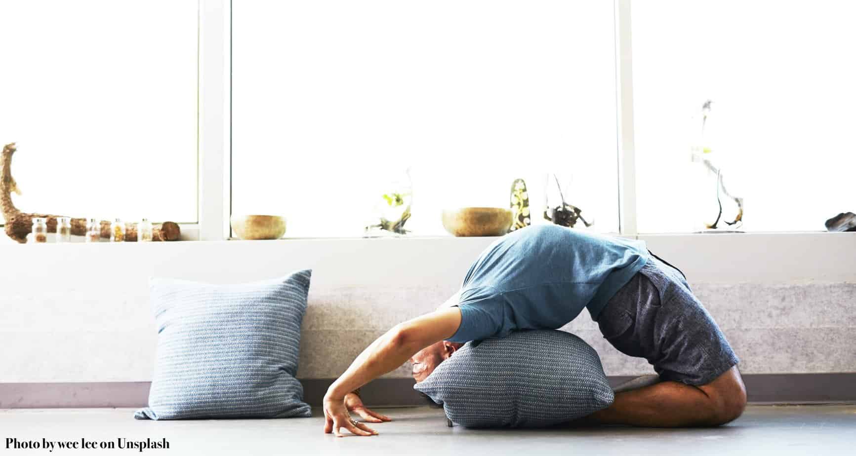 a white person on their knees back bending with a pillow supporting them under their upper back.