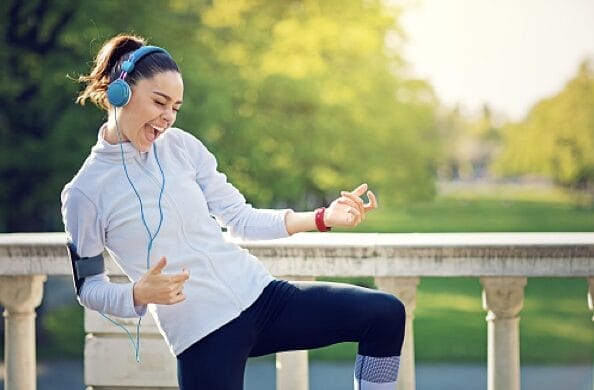 A person with a ponytail wearing teal head phones rocking out. They wear workout clothes and seem excited.